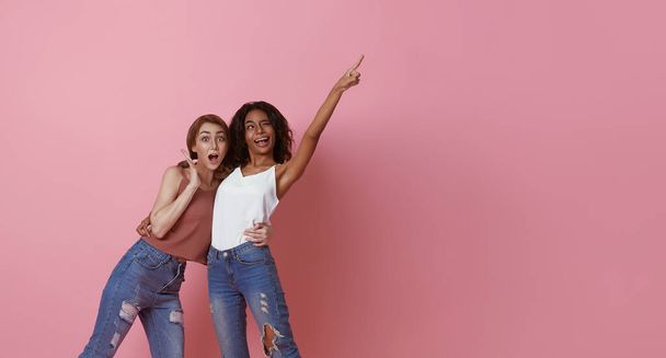 Happy loving lesbian couple good time together with finger pointing to copy space isolated on pink background. LGBT concept. - 写真・画像