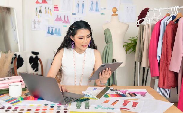 Красивий азіатський дизайнер моди малює ескізи для нової колекції на комп'ютерному ноутбуці. Студія дизайнерської творчої майстерні
. - Фото, зображення