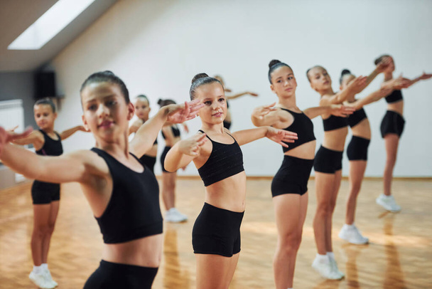 Standing and doing synchronised moves. Group of female kids practicing athletic exercises together indoors. - Foto, afbeelding