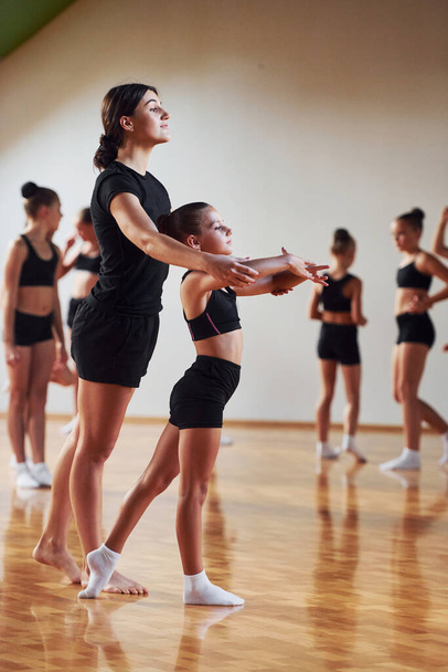 Woman teaching and helping. Group of female kids practicing athletic exercises together indoors. - 写真・画像