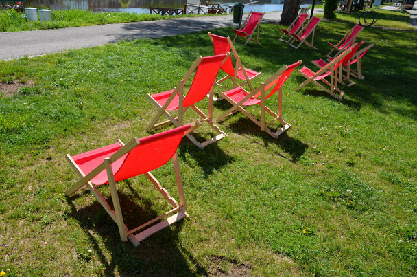 skupina skládacích dřevěných houpacích židlí na trávníku v uličce před restaurací u řeky na nábřeží. cyklostezka přináší cyklisty na studené nápoje a odpočinek. opalovací dívka - Fotografie, Obrázek