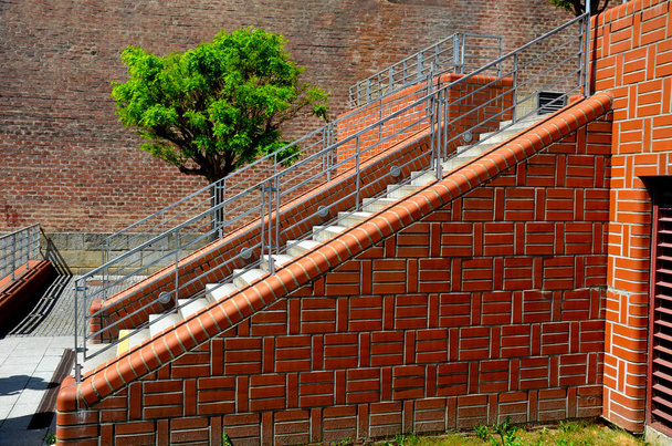 Treppen und Geländer aus freigelegten Ziegelsteinen glatte Oberfläche. Metallgeländer und Bänke in den Ecken der U-förmigen gemauerten Stützmauern. Die Einbauleuchten beleuchten die Füße der Fußgänger unter den Füßen - Foto, Bild