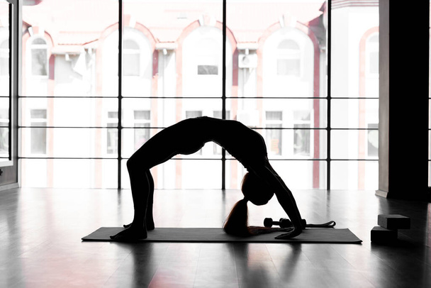 Silhouette einer Yogi-Frau, die Ellenbogenbrücke Übungen macht, Dwi Pada Viparita Dandasana Pose, Training in der Turnhalle auf dem Hintergrund des Fensters, Sportbekleidung, gesundes Lifestyle-Konzept. Kopierraum. - Foto, Bild