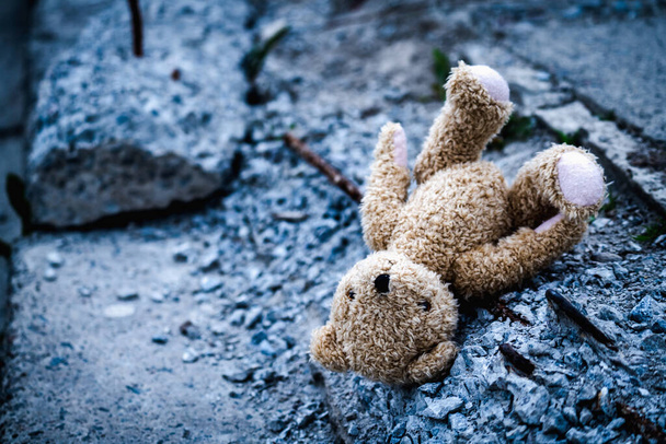 Fogalmi kép: gyermekkor és jövő elvesztése. Gyermek játék mackó fekszik törött építési törmelék hátterében elpusztult épület. - Fotó, kép
