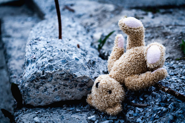 Konzeptbild: Russlands Krieg gegen die Ukraine. Kinderspielzeug-Teddybär liegt auf zerbrochenem Bauschutt vor dem Hintergrund zerstörter Gebäude. - Foto, Bild