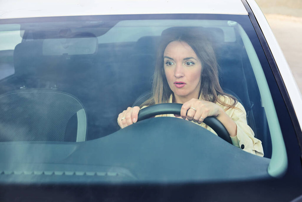Young woman driving a car and frightened looks at the road through the windshield. The concept of danger on the road and inattentive car driving - Photo, Image
