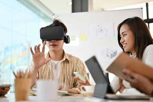 Milenijny Azjata grający w grę VR, noszący słuchawki VR, próbujący nowej innowacyjnej gry w biurze. - Zdjęcie, obraz