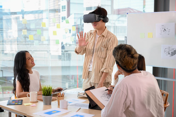 A man wearing a VR glasses to test a new virtual innovation experience in the meeting. A group of tech developers meeting in the office. - Photo, Image