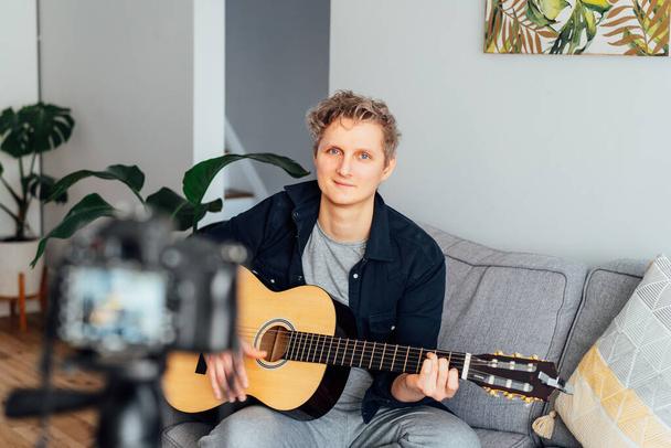 Young man playing acoustic guitar and recording music video for his social networks. Amatuer musician create content at home by modern camera. Musician blogger singing song. hobby activity concept. - Valokuva, kuva
