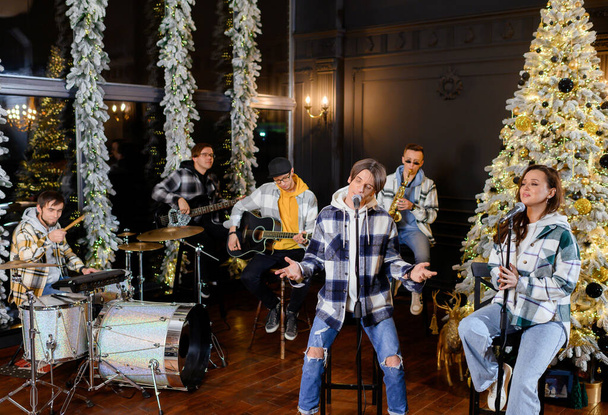 Joven banda de rock canta y toca en el fondo del árbol de Navidad  - Foto, Imagen