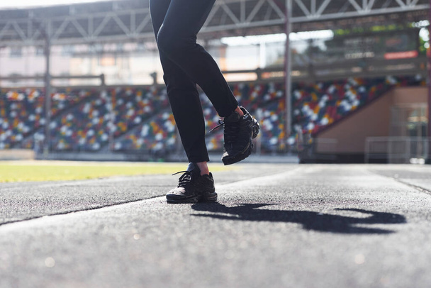 Close up view of legs of runner in black pants and shoes that is outdoors on the track. - Fotografie, Obrázek