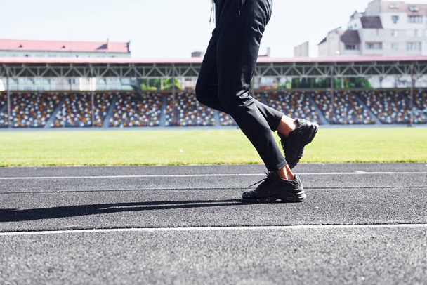 Close up view of legs of runner in black pants and shoes that is outdoors on the track. - Fotografie, Obrázek