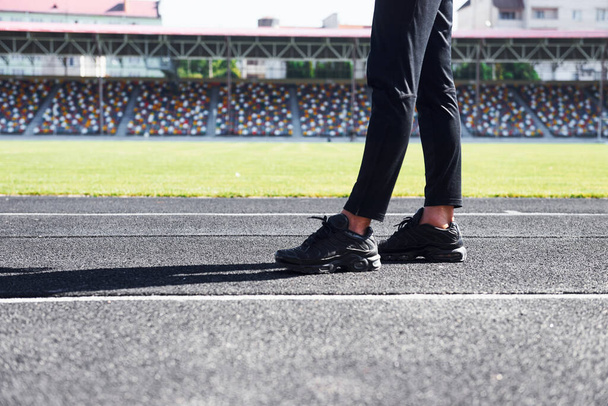 Close up view of legs of runner in black pants and shoes that is outdoors on the track. - Foto, afbeelding