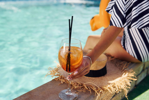 Young woman sits near swimming pool at daytime with cocktail. - Foto, Bild