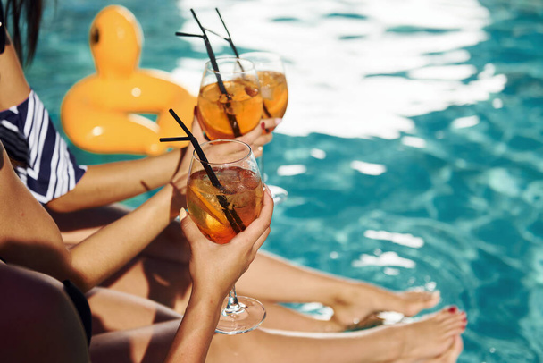 Fresh cocktails in hands. Group of young happy people have fun in swimming pool at daytime. - Фото, зображення