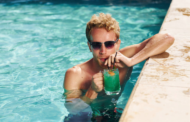 Guy in black sunglasses and with cocktail is in swimming pool. - 写真・画像