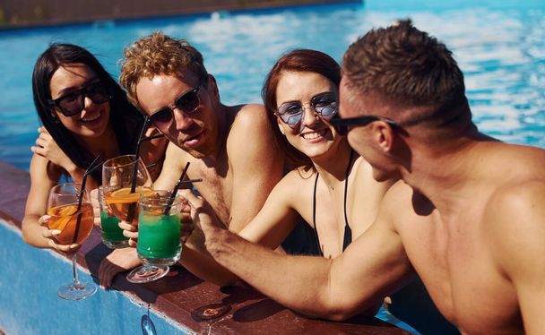 Talking and drinking. Group of young happy people have fun in swimming pool at daytime. - Fotó, kép