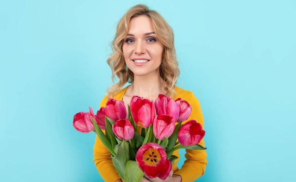 青を背景に春のチューリップの花を持つ陽気な若い女性。3月8日 - 写真・画像