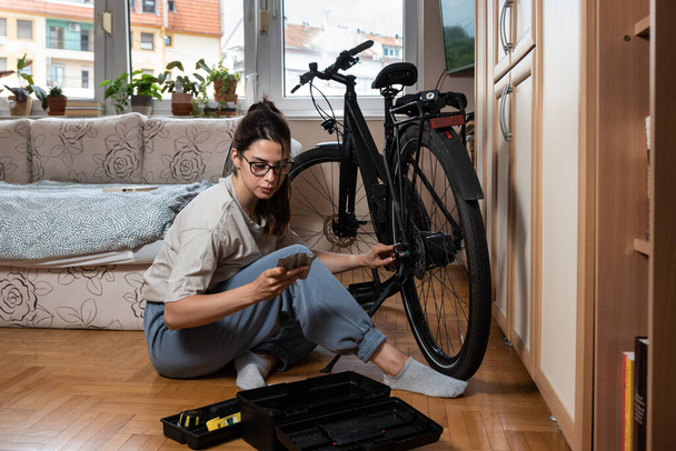 Young self learned woman or girl mechanic fixing and repairing her bicycle at her home. Female repair chain on rear wheel before she start to ride a bike on nice sunny weather.  - Фото, изображение