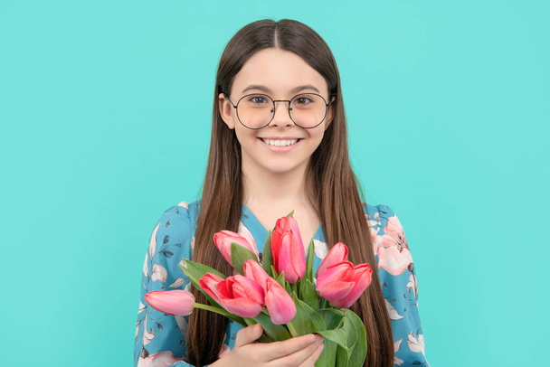 веселый детский портрет в очках с тюльпанами. День матери или женщины. ребенок держать цветы - Фото, изображение