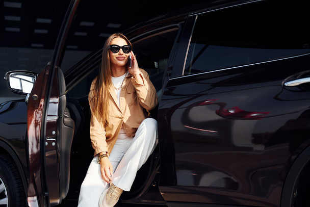 Enjoying fresh air. Fashionable beautiful young woman and her modern automobile. - 写真・画像