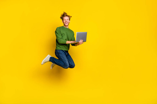Full length photo of impressed cute man wear pullover jumping modern gadget empty space isolated yellow color background - Fotografie, Obrázek