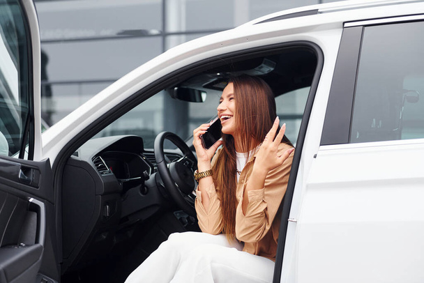 Talks by phone with door opened. Fashionable beautiful young woman and her modern automobile. - Photo, Image
