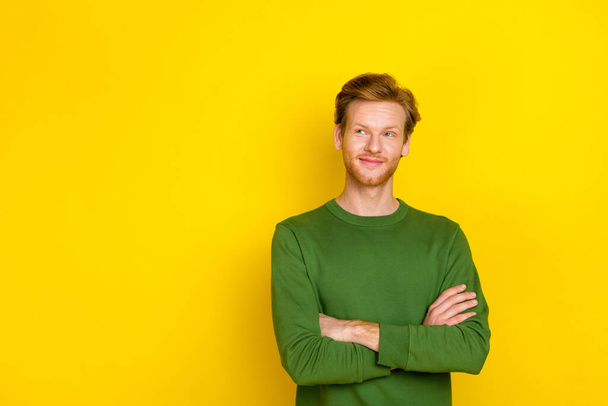 Photo of dreamy cute guy dressed green sweater arms folded looking empty space isolated yellow color background - Fotoğraf, Görsel