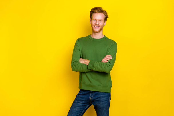 Fénykép bájos csinos férfi viselni zöld pulóver karok keresztbe üres tér elszigetelt sárga szín háttér - Fotó, kép