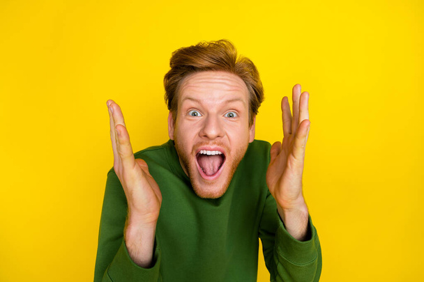 Photo of funky impressed guy dressed green sweater open mouth rising arms isolated yellow color background - Фото, изображение