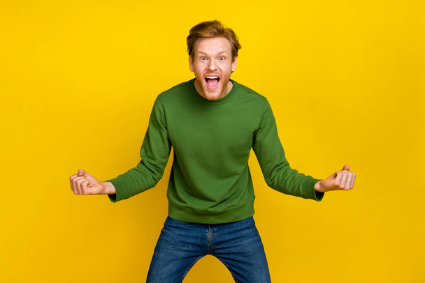 Photo of impressed lucky guy dressed green sweater smiling rising fists isolated yellow color background - Φωτογραφία, εικόνα