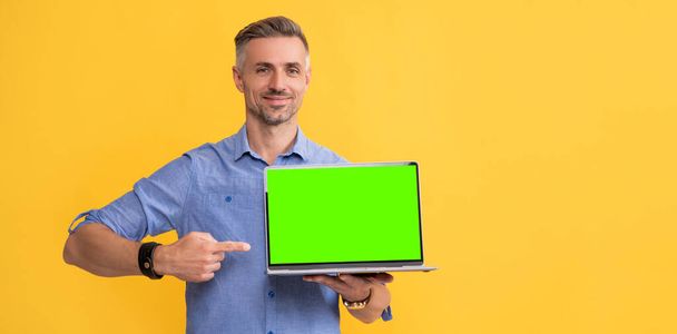 黄色の背景にノートパソコンの指を指す成熟した男,コピースペース,ビジネスウェビナー - 写真・画像