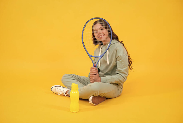 enfant heureux assis dans des vêtements de sport avec raquette de courge et bouteille d'eau sur fond jaune, enfance - Photo, image