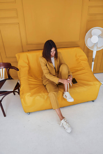 Woman sits indoors in orange colored room. In same colored clothes. - Foto, Bild