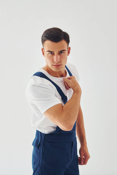 Shows biceps. Ready to work. Male worker in blue uniform standing inside of studio against white background. - Foto, Bild