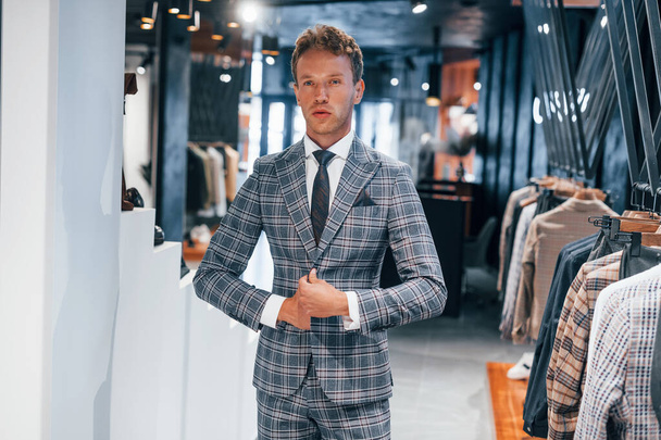Tries on wear. Young guy in modern store with new clothes. Elegant expensive wear for men. - Foto, afbeelding