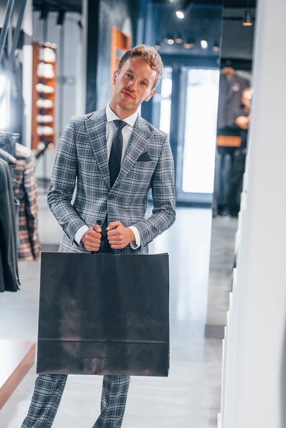 Holds bag with purchase. Young guy in modern store with new clothes. Elegant expensive wear for men. - Fotoğraf, Görsel