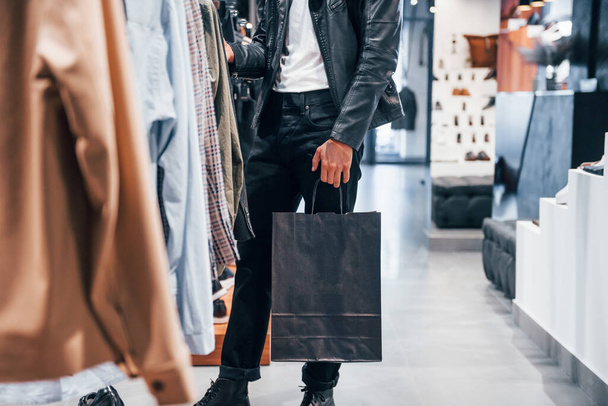 Particle view. Young guy in modern store with new clothes. Elegant expensive wear for men. - Foto, imagen
