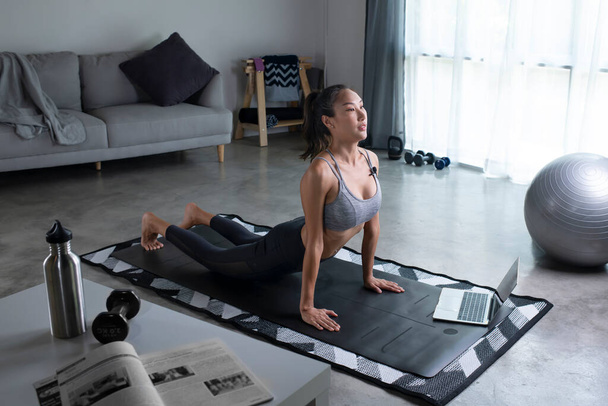 Desportivo jovem mulher asiática prancha na frente do laptop, sala de estar interior, vista lateral, espaço de cópia. Jovem saudável no sportswear exercício em casa, assistindo aula de fitness online - Foto, Imagem