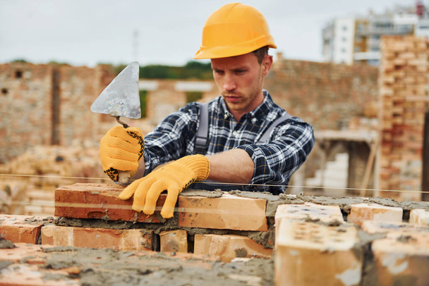 Laying bricks. Construction worker in uniform and safety equipment have job on building. - Фото, изображение