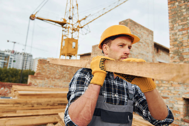 Transporting wooden boards. Construction worker in uniform and safety equipment have job on building. - Foto, imagen