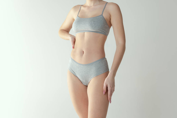 Cropped studio shot of tender slim female body in comfrotable underwear isolated over grey background - Fotoğraf, Görsel