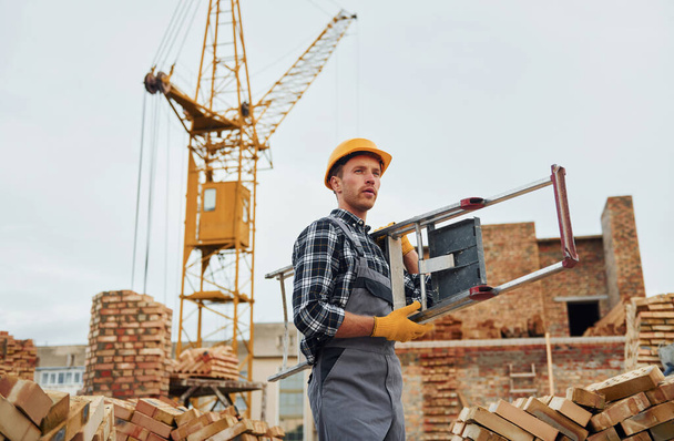 Ladder in hands. Construction worker in uniform and safety equipment have job on building. - Foto, Imagem