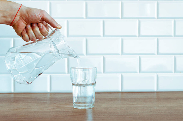 Выливание чистой пресной воды из кувшина в стекло на стол - Фото, изображение