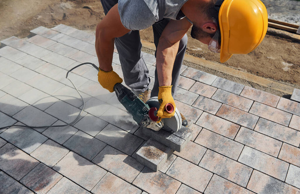 Uses circular saw. Male worker in yellow colored uniform have job with pavement. - 写真・画像
