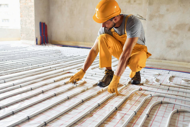 Worker in yellow colored uniform installing underfloor heating system. - Foto, Imagem