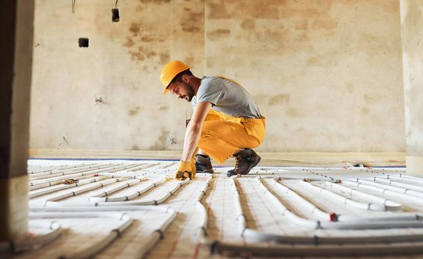 Worker in yellow colored uniform installing underfloor heating system. - Foto, imagen