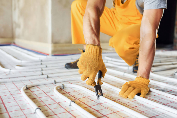 Close up view. Worker in yellow colored uniform installing underfloor heating system. - Foto, afbeelding