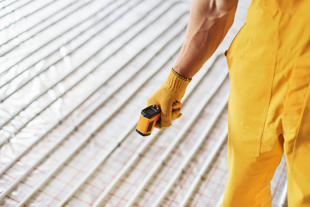 Vue rapprochée. Travailleur en uniforme de couleur jaune installant le système de chauffage par le sol. - Photo, image