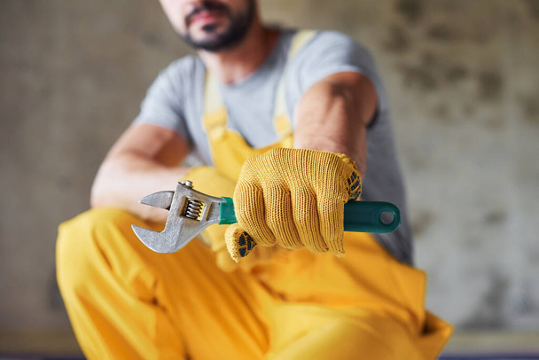 Mantiene la llave en la mano. Trabajador en uniforme de color amarillo instalando sistema de calefacción por suelo radiante. - Foto, imagen